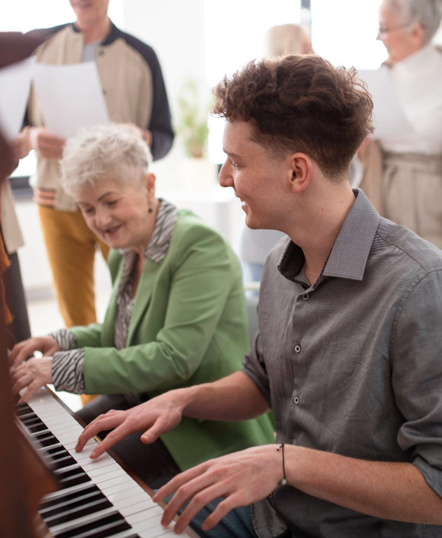 young adult and senior sitting on piano bench smiling, playing piano